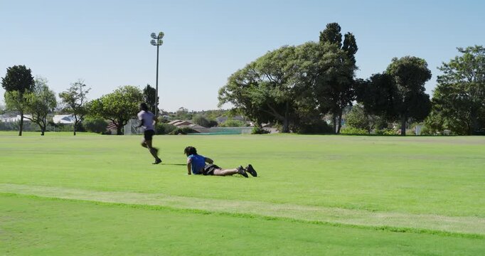 Diverse male friends in sportswear tossing ball at park, chasing, diving for friendly game