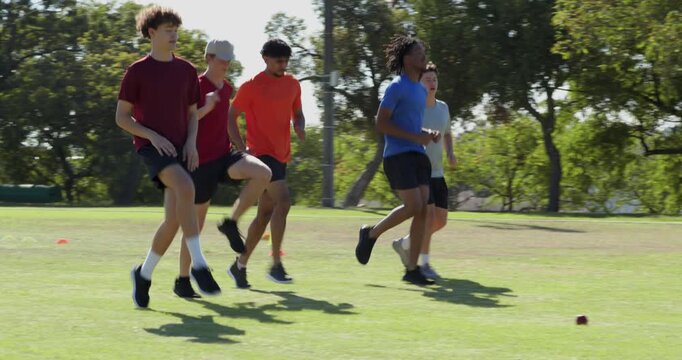 On unshown cue five male trainees side-shuffling past cones on turf field practicing agility