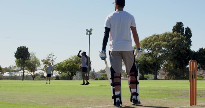 Diverse group running and bowling on grassy field batsman hitting ball to score runs