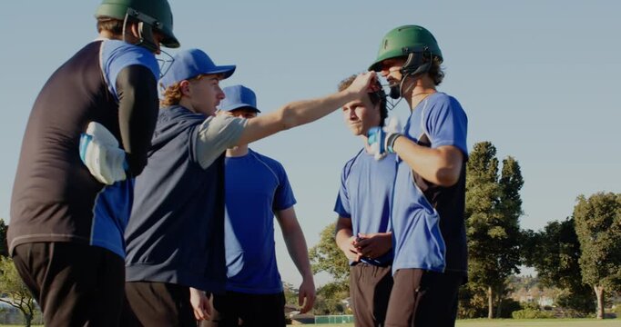 Huddling male coach and players in blue jerseys on baseball field, with whistle, helmets, glove