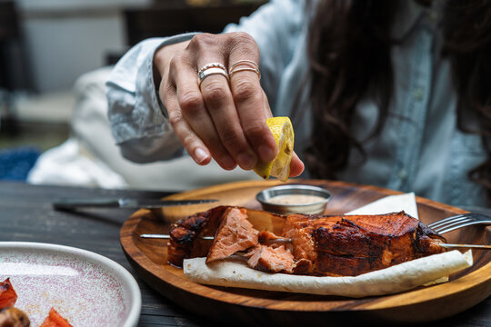 Cropped hand of a person squeezing fresh lemon juice over grilled salmon steak