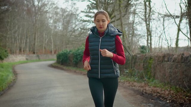 Cardio focused female running on curved rural road surrounded by forest scenery. Sporty woman maintaining pace increasing stamina and supporting heart health. Dynamic outdoor workout reflecting
