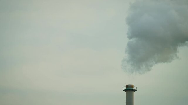 Industrial smokestack releasing thick smoke into overcast sky. Factory air pollution, harmful emissions and environmental contamination concept. Industrial air pollution risks and climate impact
