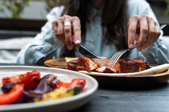 Cropped hands of a person cutting grilled salmon steak with knife and fork at an outdoor restaurant