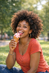 Fototapeta premium Smiling woman with curly hair sitting and eating ice cream cone. Casual summer outfit in park.