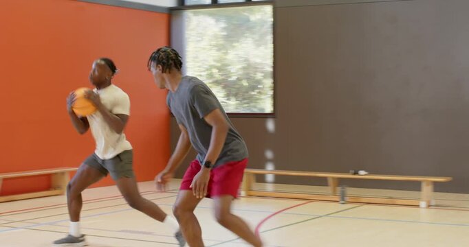 Asian coach blowing whistle timing drill at hoop as black male players dribbling and rebounding