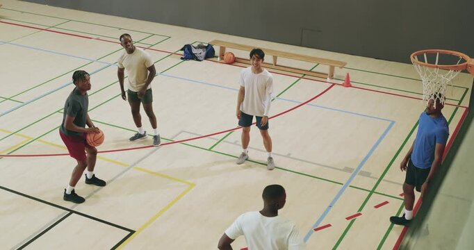 Receiving pass, diverse male friends passing ball then shooting and regrouping in gym during play