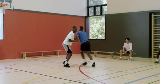 African american male team dribbling basketball using crossovers on gym court toppling defender