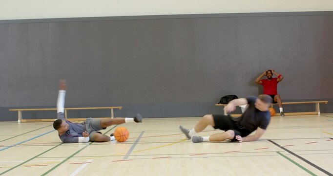 Training partners dribbling basketball on court after crossover colliding falling helping
