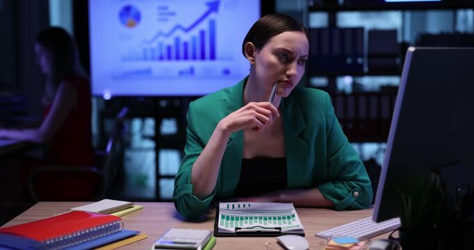 Doubted businesswoman finds solution of complicated problem in evening office. Female employee prepares financial report on computer in workplace