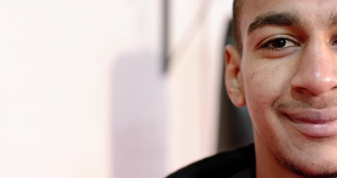 Man blinking and smiling, shifting gaze back at camera against pale interior wall, copy space