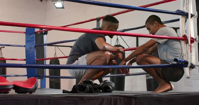 Male coach and trainee sharing and bumping fists after exhaustion, crouching in ring to motivate