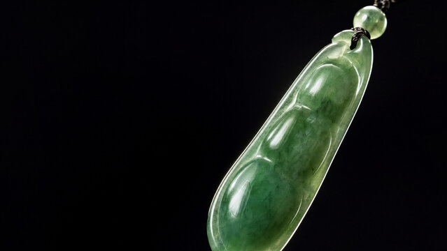 A slender green jade pendant shaped like a silique on a dark background