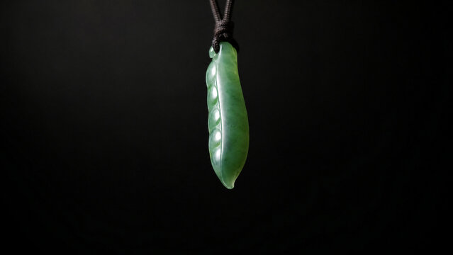A slender green jade pendant shaped like a silique on a dark background