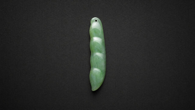 A slender green jade pendant shaped like a silique on a dark background