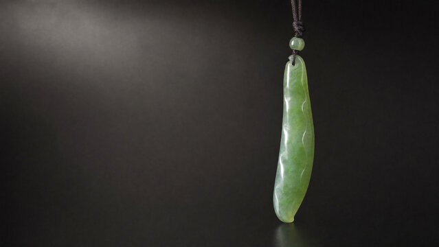 A slender green jade pendant shaped like a silique on a dark background