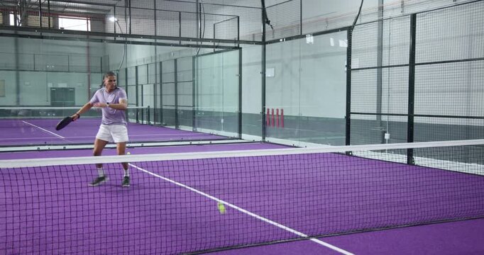 Man swinging black racket at fed ball, jogging, lunging forehand and practicing strokes on court