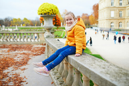 Young girl sitting on a stone balustrade in Jardin du Luxembourg in Paris, France, illustrating childhood, family travel, autumn sightseeing, and seasonal outdoor leisure