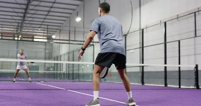 Following rival launching pickleball shot, male opponents rallying backhand volleys on padel court
