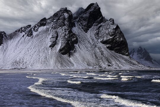 White foamy waves on the beach of Stokkness, behind snowy rocky slopes of Vestrahorn, near H&ouml;fn, Sudausturland, Iceland