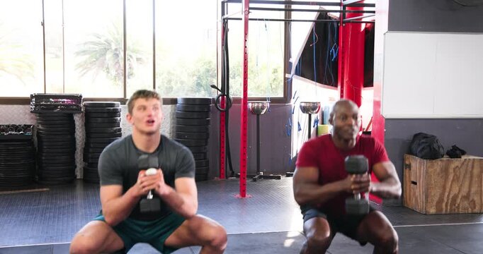 Holding chest-level dumbbells, training partners performing goblet squats in crossfit gym