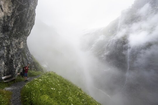 Mountaineer hiking on a hiking trail on a steep rock face, hiking to Berghaus B&auml;regg, cloud-covered rock gorge with waterfall, Bernese Alps, Bernese Oberland, Switzerland
