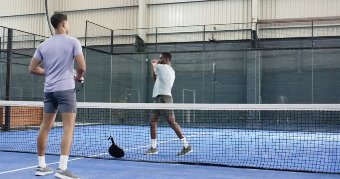 Diverse male friends placing racket by padel court net, warming up rackets, starting rally