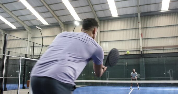 Diverse male opponents with rackets picking padel ball, tossing serve volleying on court