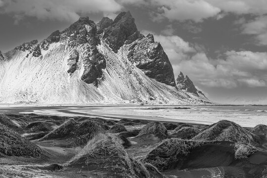 Black sand dunes with reed remains, behind them snowy rocky slopes of Vestrahorn, black and white photo, near H&ouml;fn, Sudausturland, Iceland