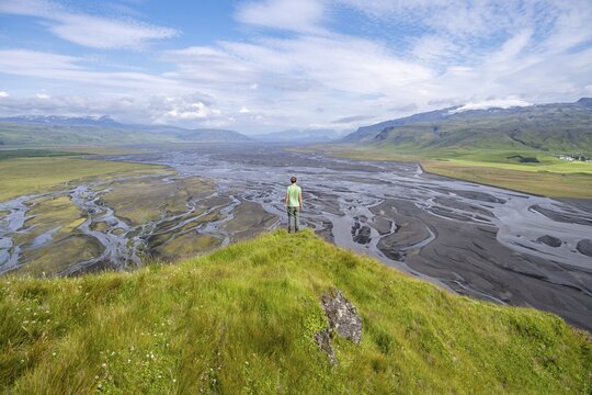 Hiker, young man on a hill, view over alluvial land, meandering river, D&iacute;monarhellir, Su&eth;urland, Iceland