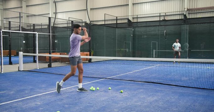 Lobbing ball by player b, male training partners volleying padel balls across net in drill