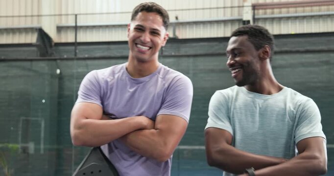 Diverse male padel friends entering court holding rackets, exchanging smiles, posing back-to-back