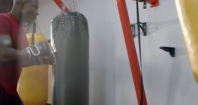 Diverse male training partners shadowboxing at gym, hitting heavy bags to sharpen technique
