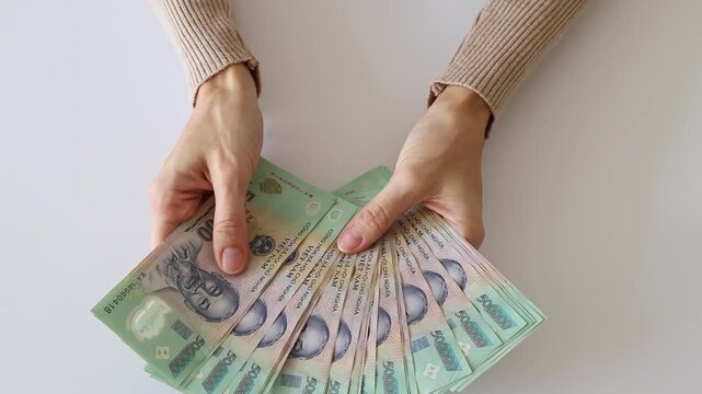Vietnamese dong currency cash money close up. Person holding a fan of green five hundred thousand VND banknotes featuring Ho Chi Minh portrait over a plain white background, top view.