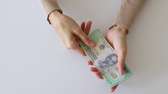 Vietnamese dong currency cash money close up. Person hands counting or flipping through a stack of green five hundred thousand VND banknotes over a plain white background, dynamic motion top view.