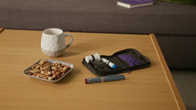 Close up on diabetes testing kit, insulin pen, and plate of mixed nuts sitting on wooden table. Clip ideal for healthcare marketing, diabetes awareness, and chronic disease management campaigns