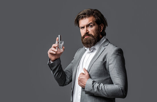 Bearded man holding up bottle of perfume. Fashion cologne bottle. Man perfume, fragrance. Masculine perfume. Male fragrance and perfumery, cosmetics