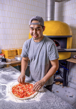 Chef makes pizza with his hands putting the ingredients for the pizza on the table. Man cook prepares a pizza in a italian restaurant pizzeria. Food, culinary, italian cuisine, cooking concept