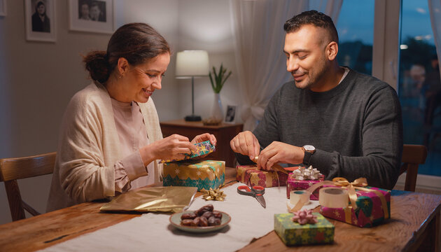 Arab parents wrapping Eid gifts at home, celebrating Ramadan with traditional Arabic cuisine and modest modern fashion, a multi-generational moment in a contemporary Middle Eastern home.