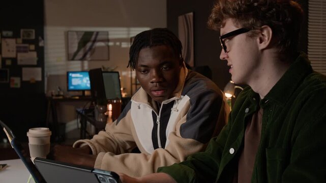 Tilt up shot of multiethnic young programmers discussing software development on tablet in office. Video for tech startup marketing, IT team collaboration, and corporate training presentations