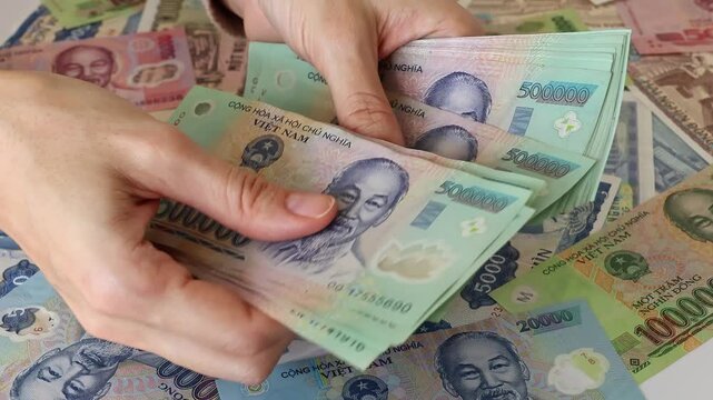 Close up view of hands counting stack of Vietnamese dong paper money bills in Vietnam. Concept of financial accounting, wealth, business budget calculation, domestic cash expenses and income tax.