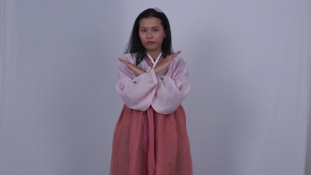 Serious Asian woman wearing traditional pink Korean hanbok dress crossing arms in X sign white background strict girl showing rejection no stop forbid gesture negative refusal commercial photo