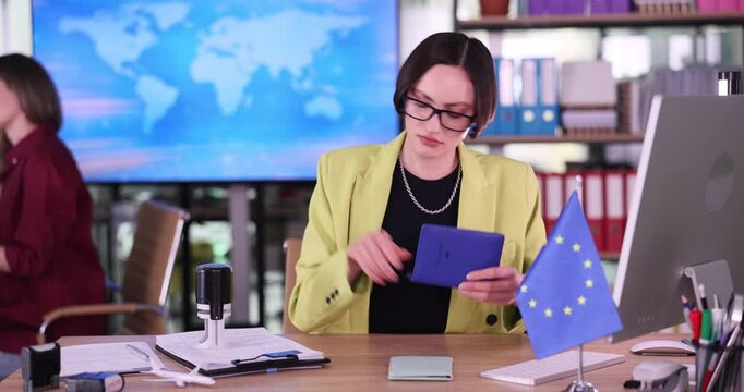 Focused embassy employee places official immigration stamps into passports. Woman consul in glasses reviews passport information in embassy office
