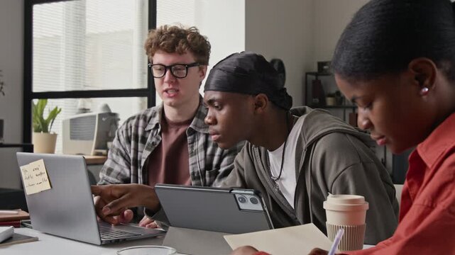 Multiethnic young adult programmers collaborating in office, Caucasian man pointing at laptop screen while Black man looking closely. Ideal for software development and tech startup marketing