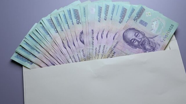 Close up view of hand holding white paper envelope filled with stack of 500000 Vietnamese dong money bills. Concept of financial bonus, bribe, corruption, secret salary and income in Vietnam.