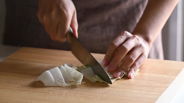 Woman hand holding kitchen knife and chopping fresh Chinese cabbage on wooden cutting board, Asian food cooking