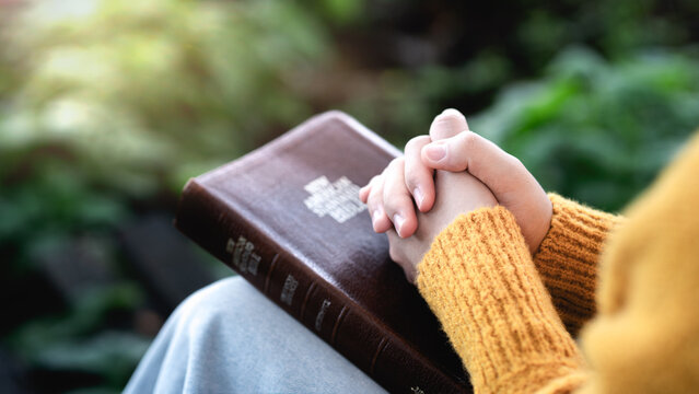 Close up of faithful woman hands clasped in prayer over Holy Bible, praying to God for hope and blessings.