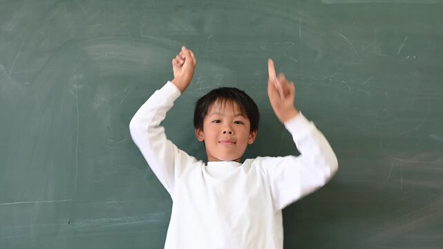 黒板の前で両手で上を指差して案内する男子小学生