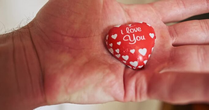 Sweet confession, man holding heart-shaped candy with I You inscription.