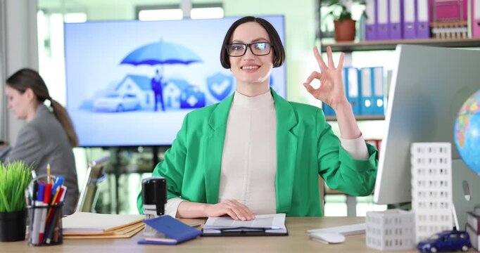 Cheerful female office worker stamps important documents and smiles warmly. Brunette woman in elegant business attire shows approving OK gesture